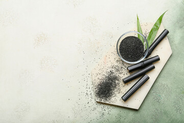 Composition with bowl of activated carbon powder, bamboo sticks and leaves on color background