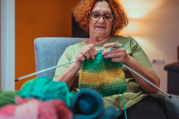 Mature woman holding knitting needles and knitting at home.