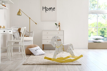 Interior of child's room with rocking horse, workplace, chest of drawers and painting on light wall