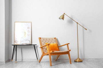 Comfortable armchair, table with beautiful painting and floor lamp in room interior