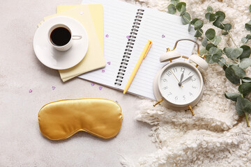 Sleep mask, notebook, cup of coffee and alarm clock on light background