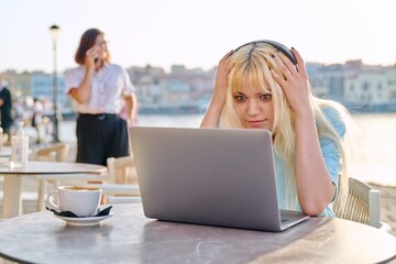 Surprised teenage female with headphones looking at laptop in outdoor cafe