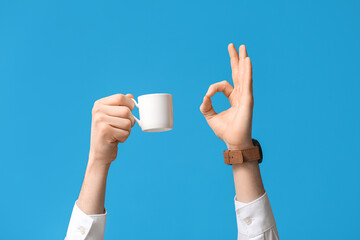Businessman with cup of coffee showing OK on blue background