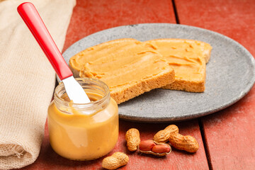 Glass with peanut butter and knife isolated on a red wooden table.