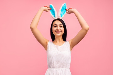 Happy young woman in bunny ears holds her ear with her hand. beautiful woman in a white dress on a...