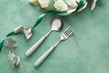 Elegant cutlery and eucalyptus leaves on green background