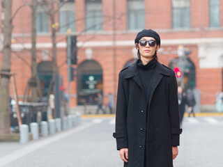 Portrait of handsome Chinese young man wearing black overcoat, sweater and trousers with sunglasses...