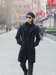 Portrait of handsome Chinese young man wearing black overcoat, sweater and trousers with sunglasses walking on Shanghai street, front view, male fashion, cool Asian young man lifestyle.