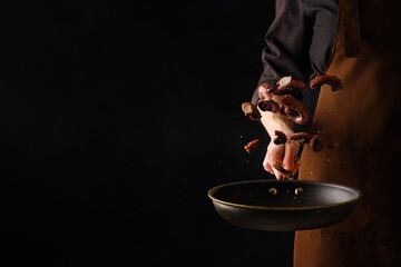 A professional chef in a dark uniform cooks octopus pieces in a pan in a frozen flight. Isolated on...