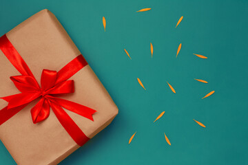 gift in craft paper and red ribbon with bow on blue background with jelly flower petals