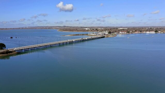Aerial footage approaching the Langstone Bridge over Langstone Harbour towards the Sailing Club on the waterfront of the harbour.