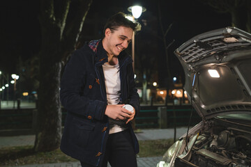 Fototapeta na wymiar One happy young adult caucasian man standing by his vehicle with open hood and broken failed engine smiling carefree hold phone calling towing service for help on the road Roadside assistance concept