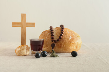 Glass of wine with bread, rosary and cross on light background