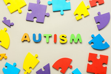 Word AUTISM with puzzle pieces on light background