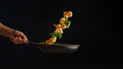Seafood - shrimps with vegetables in a frozen flight on a frying pan on a black background. Sea food. Restaurant, hotel, banquet. Advertising, banner.