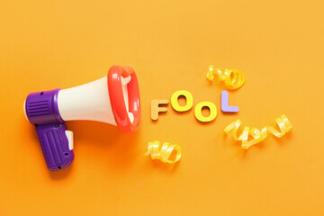 Composition with megaphone and word FOOL for April Fools Day celebration on orange background
