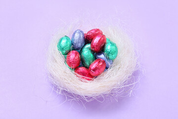 Nest with chocolate Easter eggs on lilac background