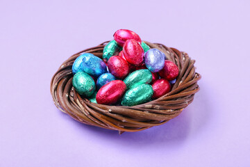 Nest with different chocolate Easter eggs on lilac background