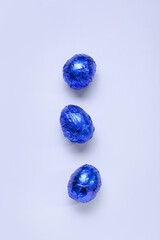 Tasty chocolate eggs in blue foil on color background
