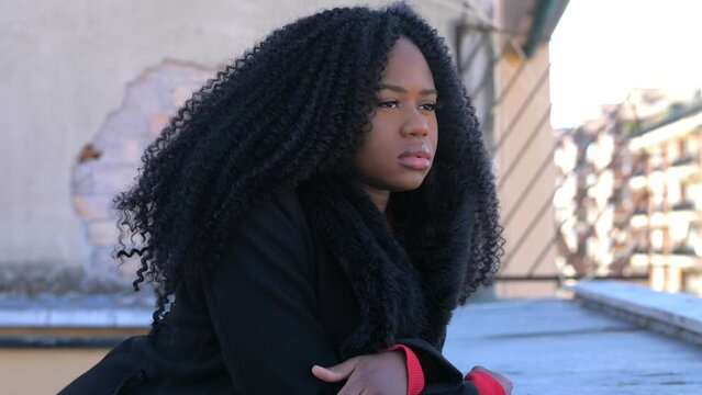 Side view of an African American mysterious disappointed resentful sad young woman leaning against the wall