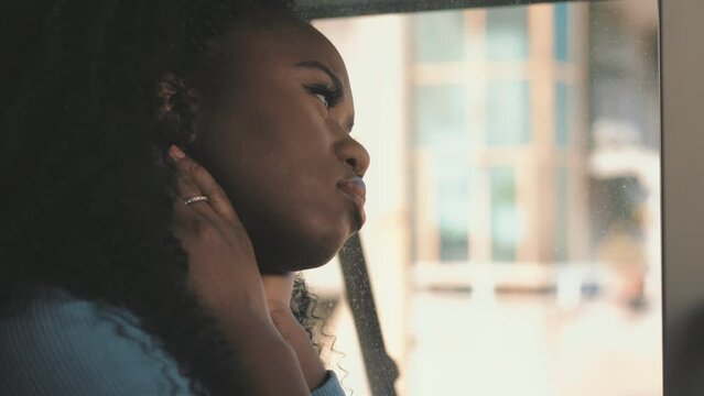 Side view of an African American mysterious disappointed resentful sad young woman looking out windows