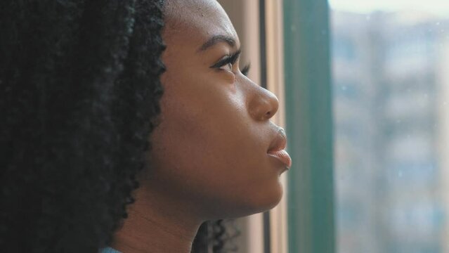 Beautiful young black woman with sad, pensive look, looking out the window