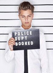 Feeling the consequences. Mug shot of a young man in a shirt and tie holding up a police department sign.