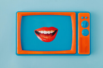 Women's lips smiling from a screen of a retro old blue and orange tv against pastel blue...