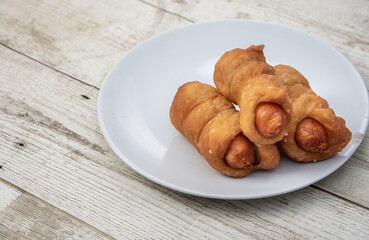 Asian street food sausage bread. On wooden floor, in white plate.