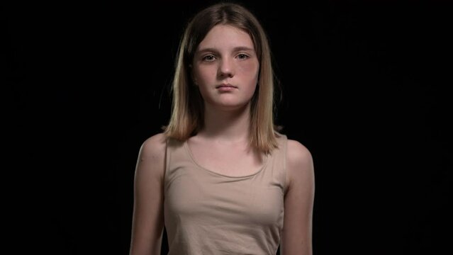 Front view bruised beaten teenage girl pushing away belt and fist looking at camera. Portrait of beaten Caucasian teenager posing at black background. Fight for freedom concept