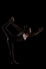 Fototapeta na wymiar Fit girl practicing yoga in a studio. Half silhouette side lit fitness model.