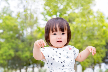 新緑の樹木を背景に笑顔で踊る幼い女の子。育児,教育,躾,愛情,幸せなイメージ