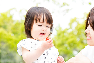 屋外で新緑の樹木を背景にブチトマトを食べる幼い女の子。食欲,幼児,自然,育児イメージ