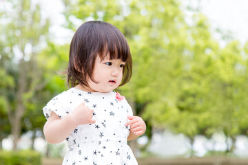 新緑の樹木を背景に笑顔で踊る幼い女の子。育児,教育,躾,愛情,幸せなイメージ