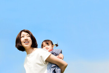 青空を背景に幼い娘を背負うお母さんのクローズアップ。母子,母性,愛情,育児のイメージ