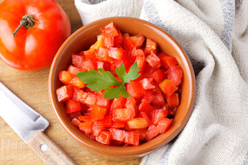 Raw chopped and diced tomatoes cubes in ceramic bowl over rustic wooden table