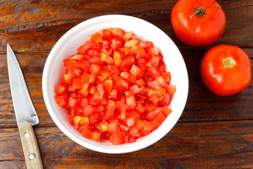 Raw chopped and diced tomatoes cubes in ceramic bowl over rustic wooden table