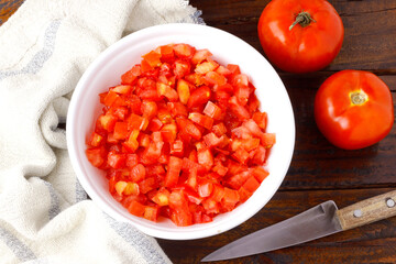 Raw chopped and diced tomatoes cubes in ceramic bowl over rustic wooden table