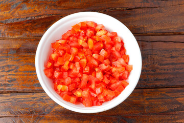 Raw chopped and diced tomatoes cubes in ceramic bowl over rustic wooden table