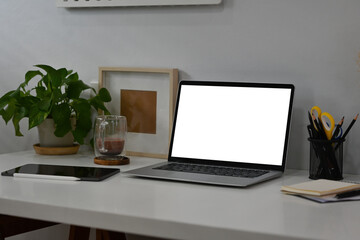 White modern office table with laptop with blank white screen, tablet, coffee cup and note books with no people, for business and technology concept.