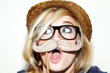 I moustache you a question.... Closeup of a young woman holding a moustache prop up to her face and looking surprised. - obrazy, fototapety, plakaty