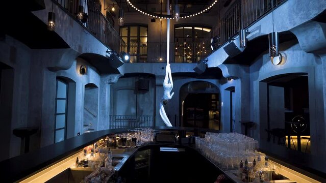 Female aerialist hanging upside down on silks with one leg, doing splits.
