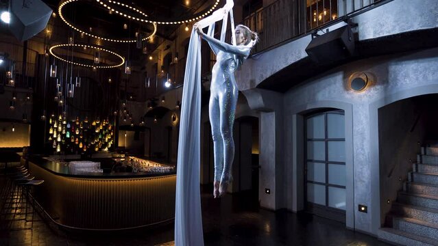 Female aerialist in the iron cross pose on silks in a music club.