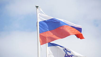 Russian and Israeli flags are weaving in the wind against bright skies