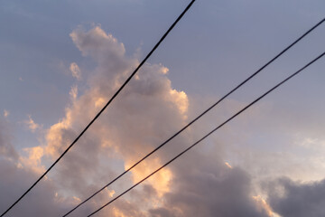 Fototapeta premium fluffy pink clouds at sunset against black telegraph wires 