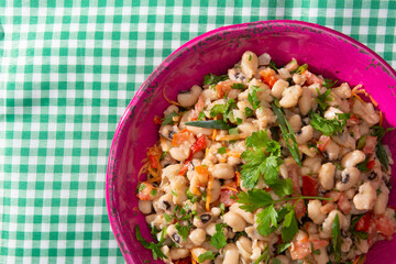 Bean salad, an homemade salad with beans, tomatoes, onions, peppers and herbs close-up on a plate on a table. Horizontal top top view