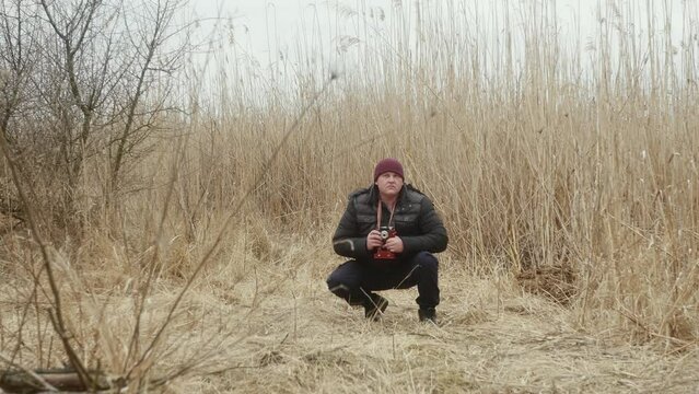 a man in nature squatting takes pictures on a vintage film camera against the background of early spring lake reeds