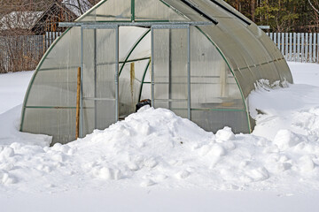 The greenhouse on the garden plot is covered with snow in early spring