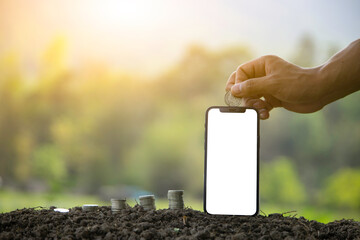 There are stacked coins lined with human hands and mobile phones against a natural green backdrop. Ideas for collecting money online or banking online.