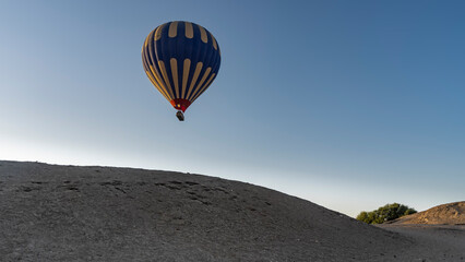 A bright yellow-blue balloon is flying in a clear sky over sand dunes. Close-up. Egypt. Luxor